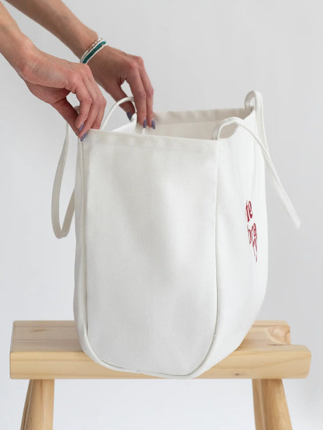 White Coastal Carryall functional tote side view on a chair with The Tote Library logo on it