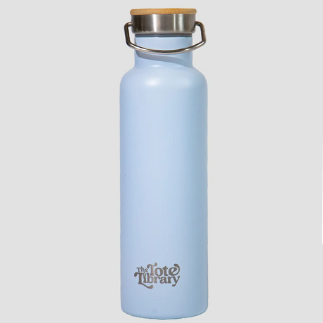 A light blue stainless steel water bottle with a bamboo-topped lid, displayed next to its packaging which has floral designs and the brand 'TTL' printed on it.
