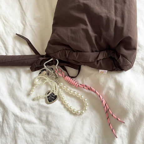 Brown drawstring bag with a keychain and pink ribbon on a white surface