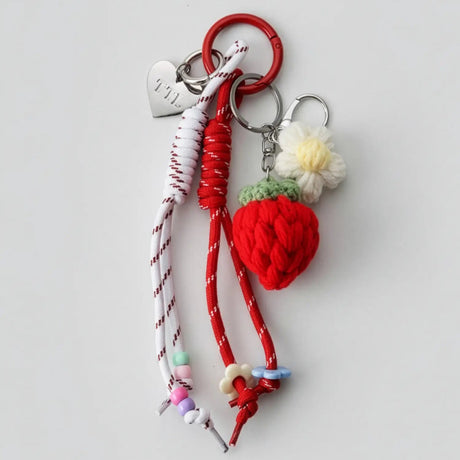 Keychain with heart-shaped charm, red strawberry, and floral decorations on a light gray background