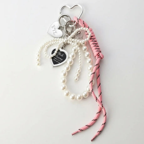 Pearl bracelet with heart-shaped charms and a pink cord on a light gray background