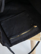 black Coastal Carryall functional tote on a chair showcasing the inside zipper pocket with The Tote Library logo on it