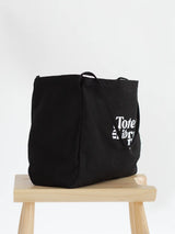 Black Coastal Carryall functional tote side view on a chair with The Tote Library logo on it