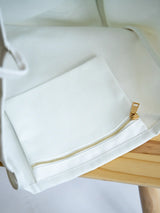 White Coastal Carryall functional tote on a chair showcasing the inside zipper pocket with The Tote Library logo on it