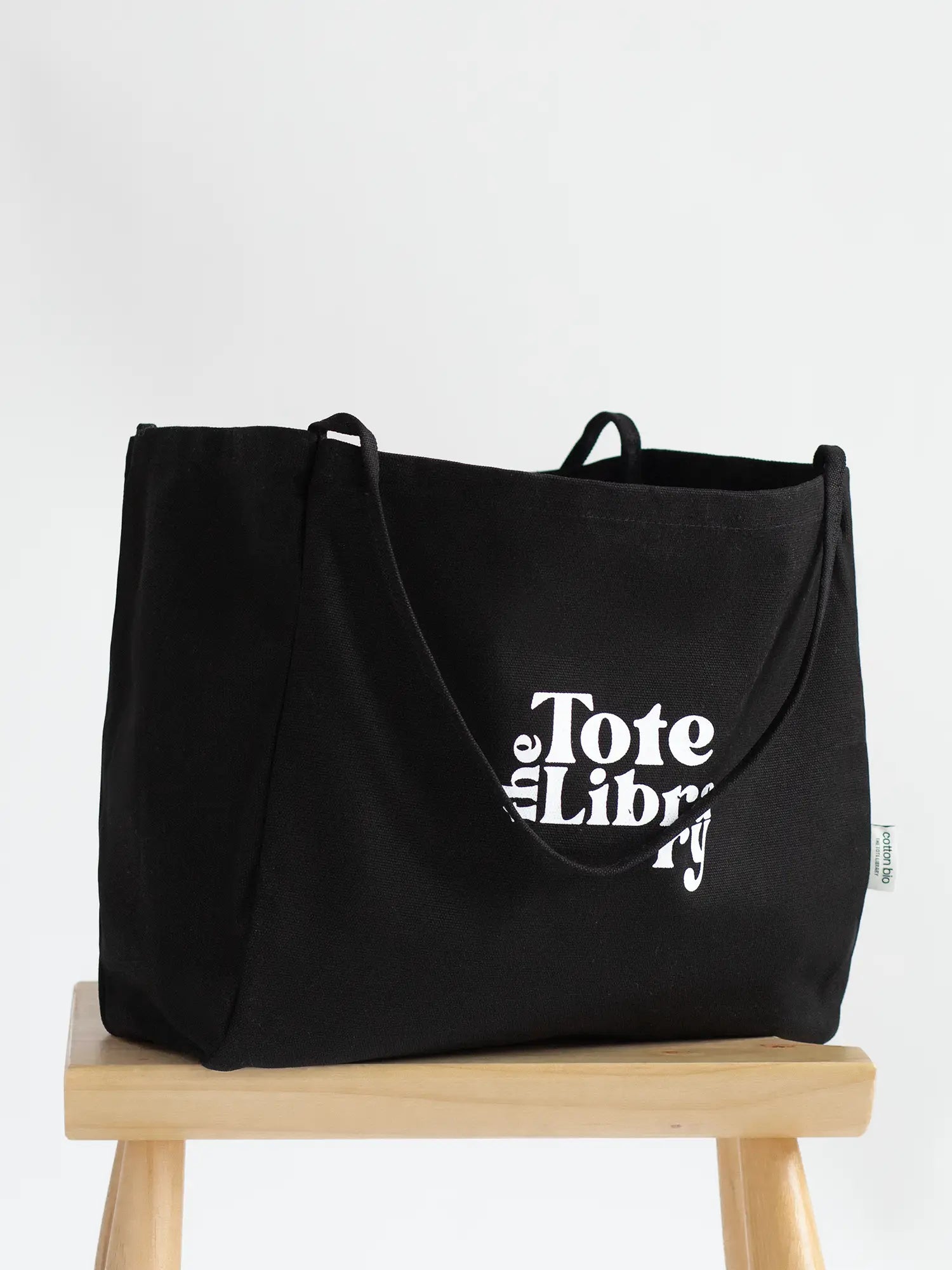 Black Coastal Carryall functional tote on a chair with The Tote Library logo on it